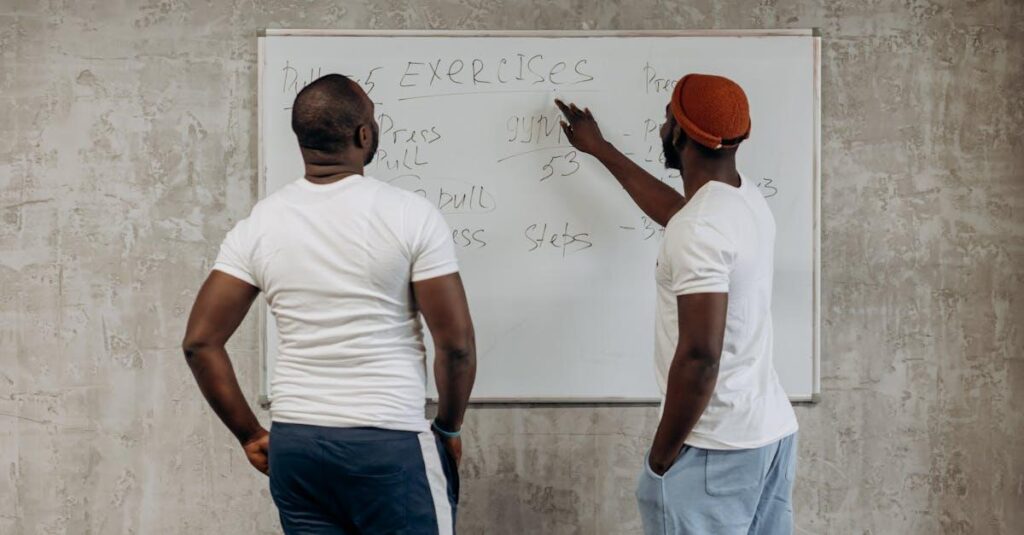 Two adult men planning their gym exercises on a whiteboard in a modern setting, emphasizing fitness and health.