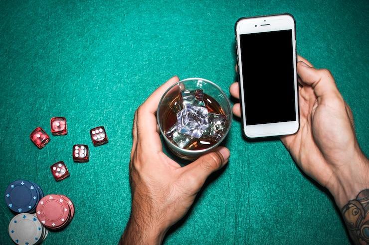 Overhead view of man's hand holding cellphone and whisky glass over the poker table